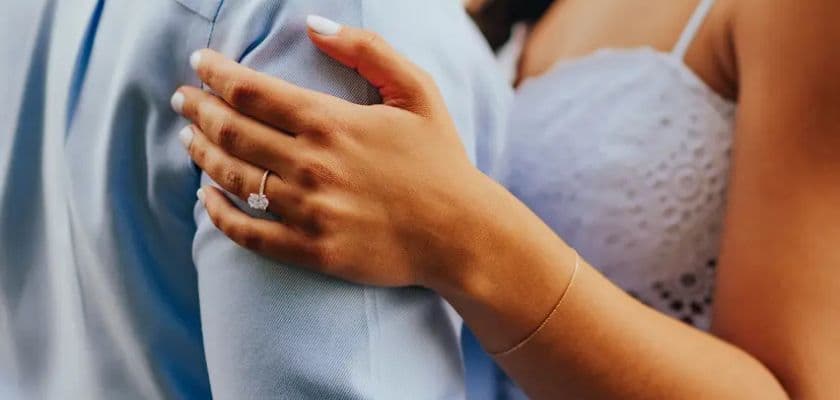 A close-up of a woman's hand with an engagement ring resting on a man's shoulder.