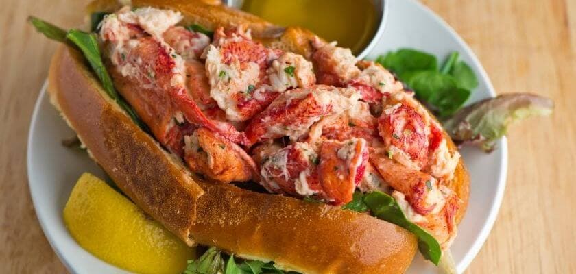 A lobster roll filled with chunks of lobster meat, served with a side of olive oil and lemon.