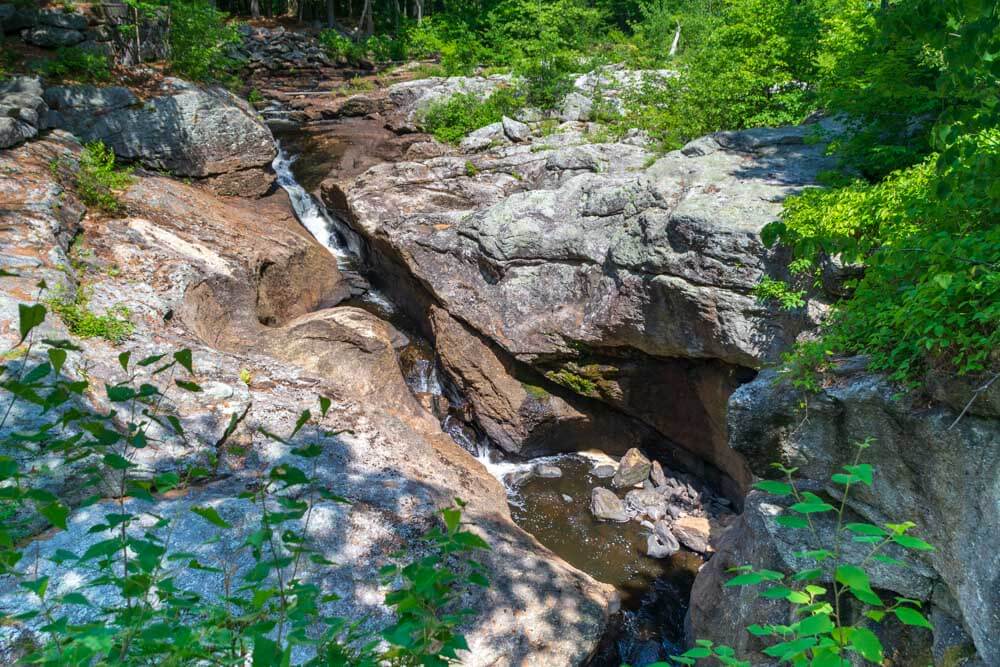 A serene landscape featuring a rocky gorge with a small stream flowing through lush greenery.