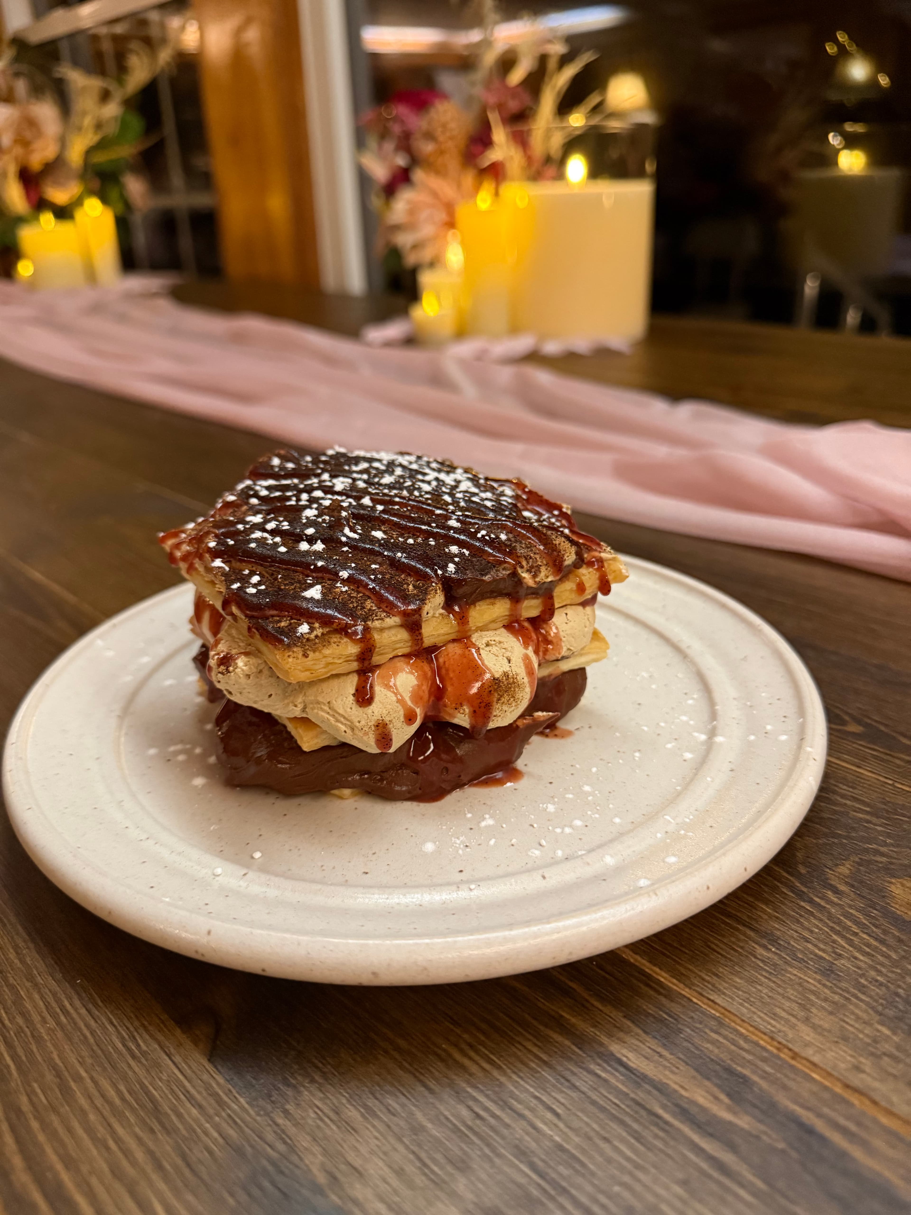 A layered dessert with chocolate, cream, and a berry sauce, dusted with powdered sugar on a plate.