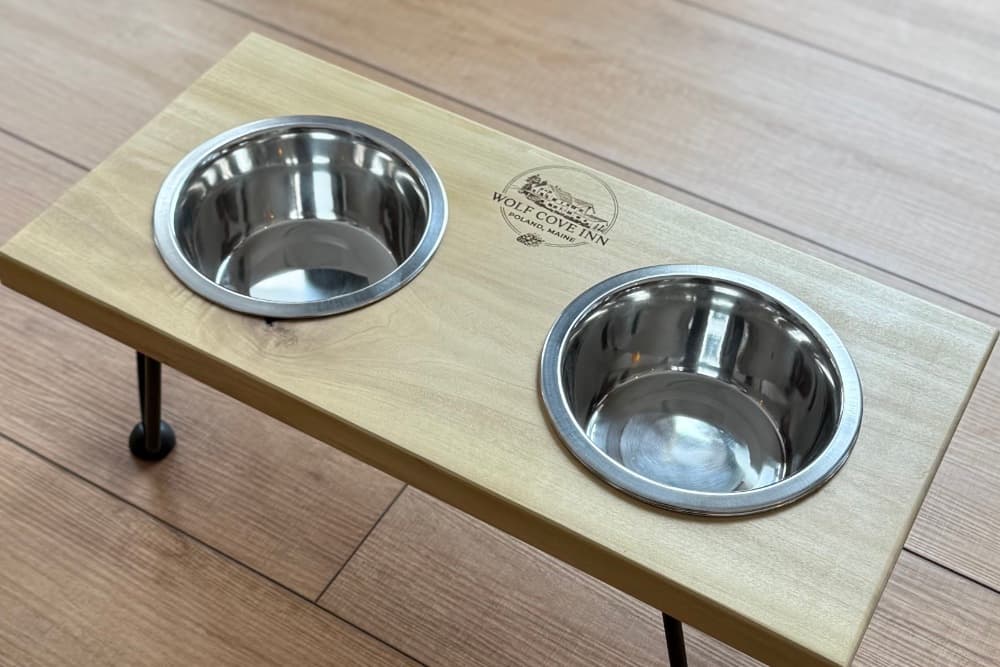 A wooden pet feeding station with two stainless steel bowls and a logo for Wolf Cove Inn.
