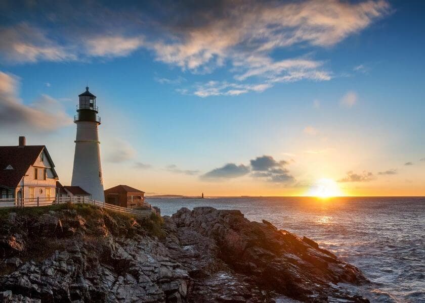 A lighthouse stands on rocky shores under a colorful sunset sky. A lighthouse stands on rocky shores under a colorful sunset sky.