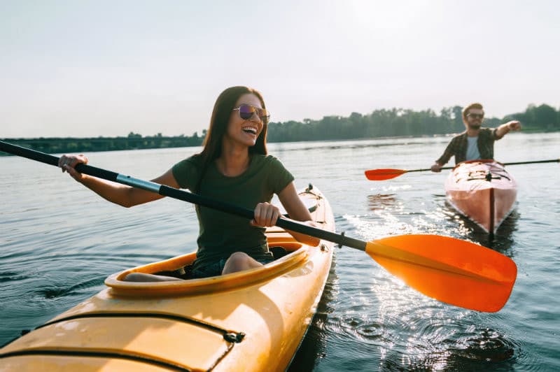 Two people kayaking on a calm lake, enjoying the sunshine and laughter.