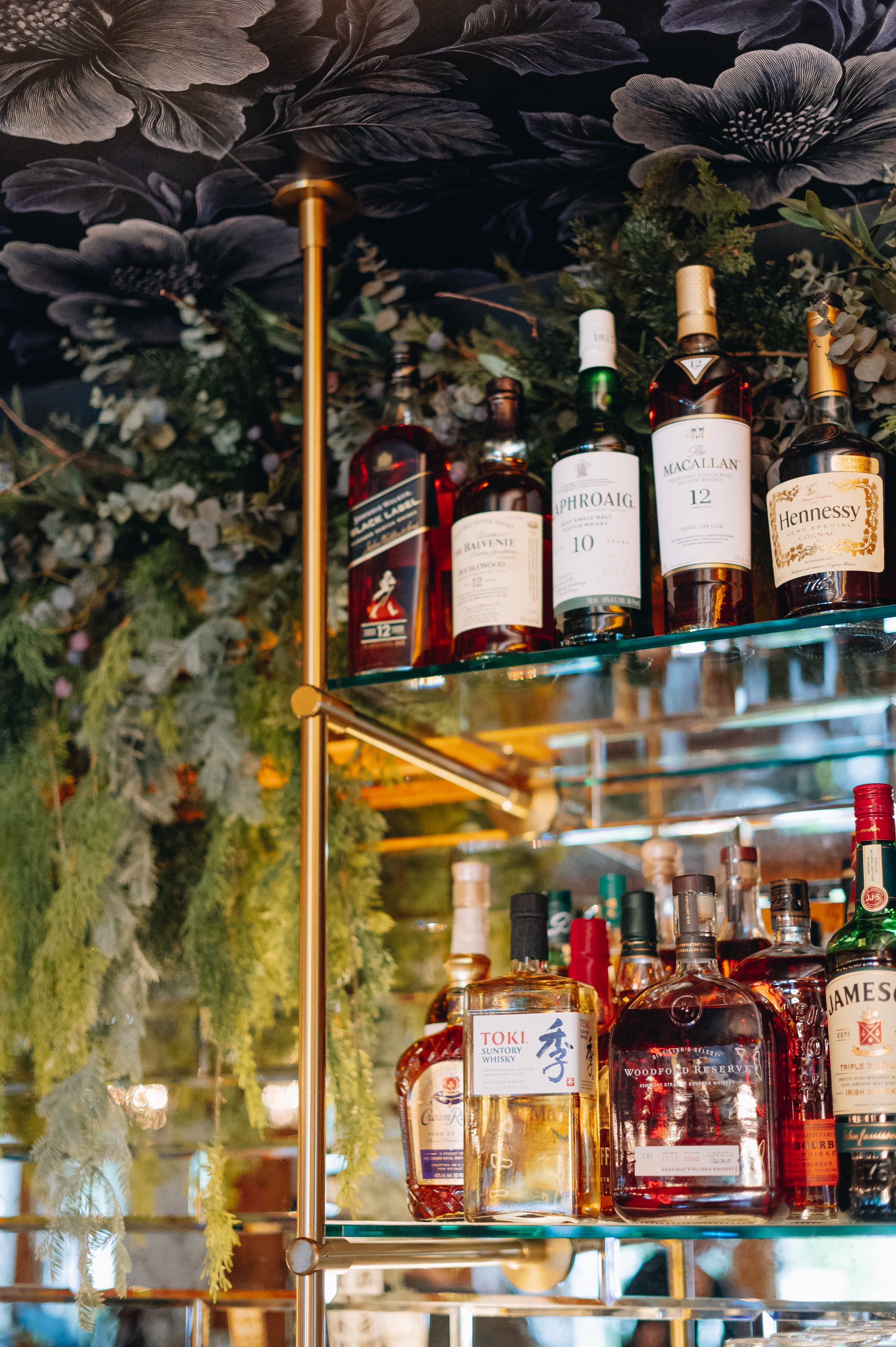 A shelf displaying various bottles of whiskey and spirits surrounded by greenery.