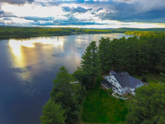 Aerial view of a lakeside house surrounded by trees under a cloudy sky.