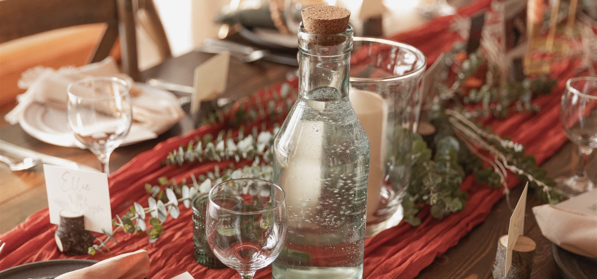 A beautifully set dining table with a glass water bottle, elegant place settings, and greenery accents.