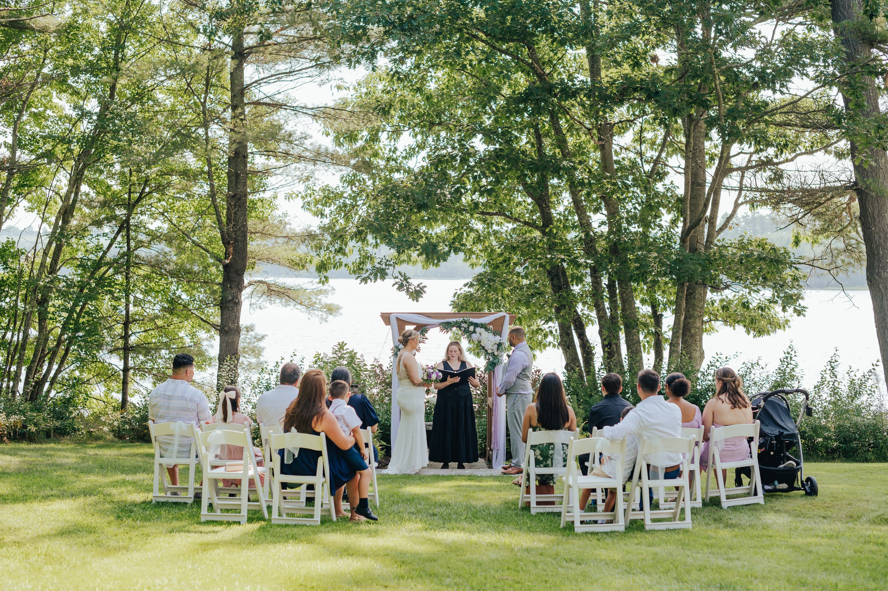 A couple exchanges vows during an outdoor wedding ceremony near a serene lake.