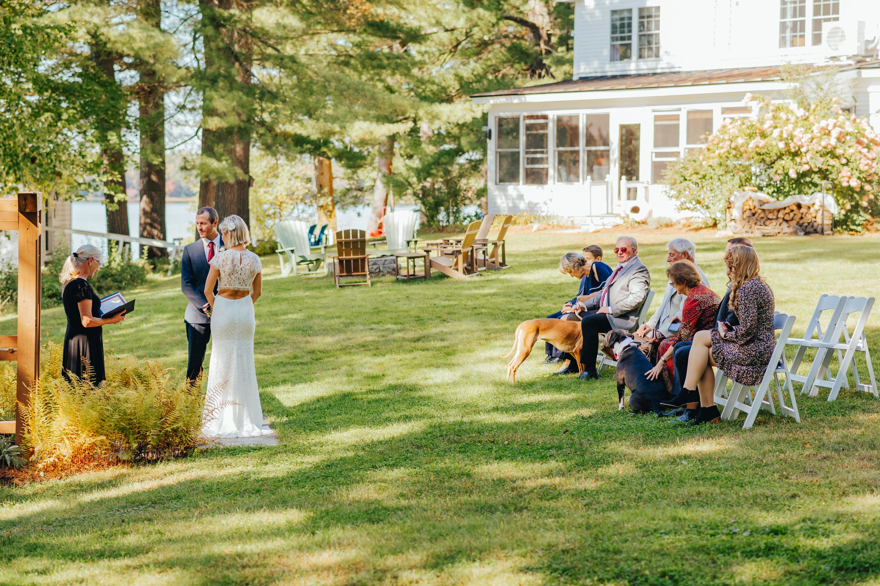 A couple stands in front of an officiant during their outdoor wedding ceremony on a sunny day, with guests seated nearby.