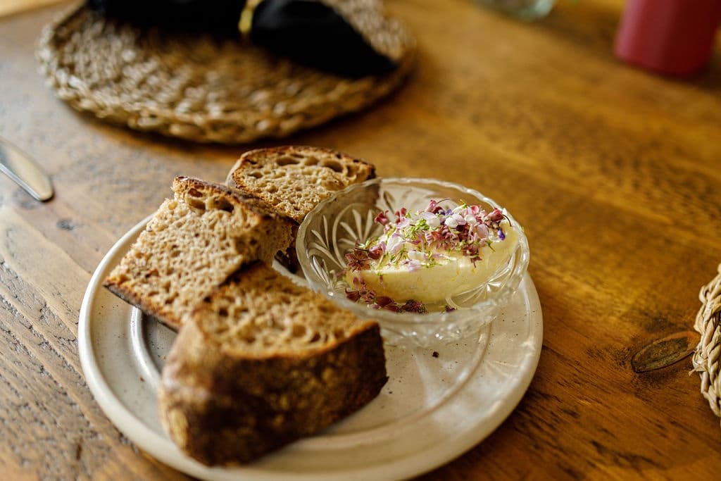 A plate of sliced bread accompanied by a small bowl of butter topped with edible flowers.