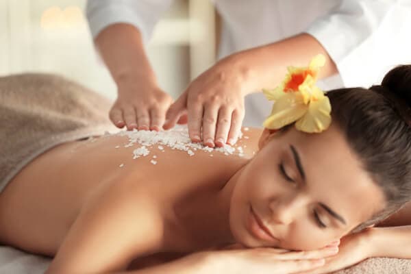 A woman relaxes during a massage, adorned with a yellow flower in her hair.