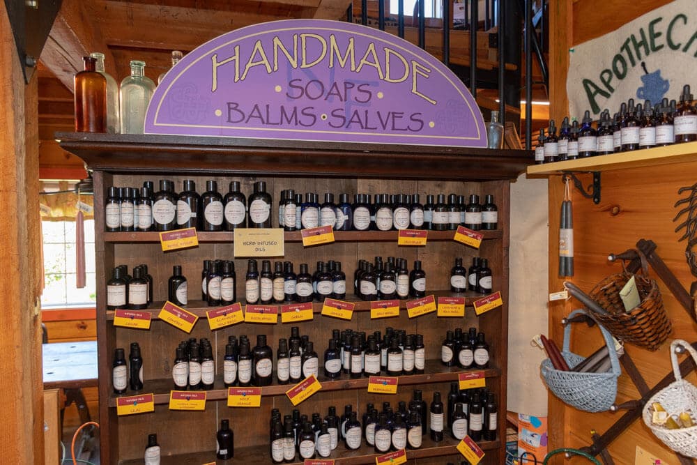 A wooden shelf displaying various handmade soap, balm, and salve bottles, complete with colorful labels.
