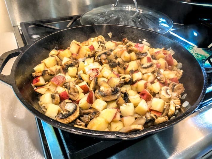 A cast-iron skillet filled with sautéed potatoes and mushrooms, steaming on a stovetop.