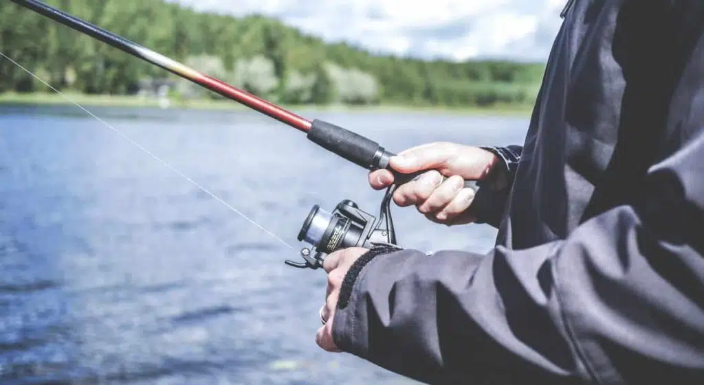 A person holds a fishing rod with a reel near a body of water.