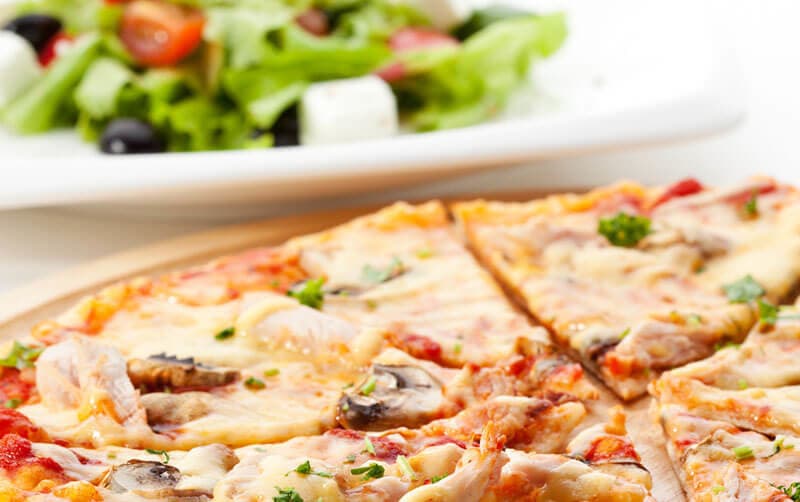 A close-up of a sliced pizza with mushrooms and herbs, accompanied by a fresh salad in the background.