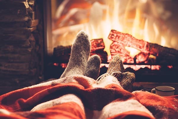 Cozy feet in warm socks under a blanket beside a crackling fireplace.