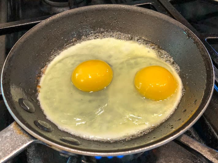 Two cracked eggs sizzling in a frying pan on a stovetop.