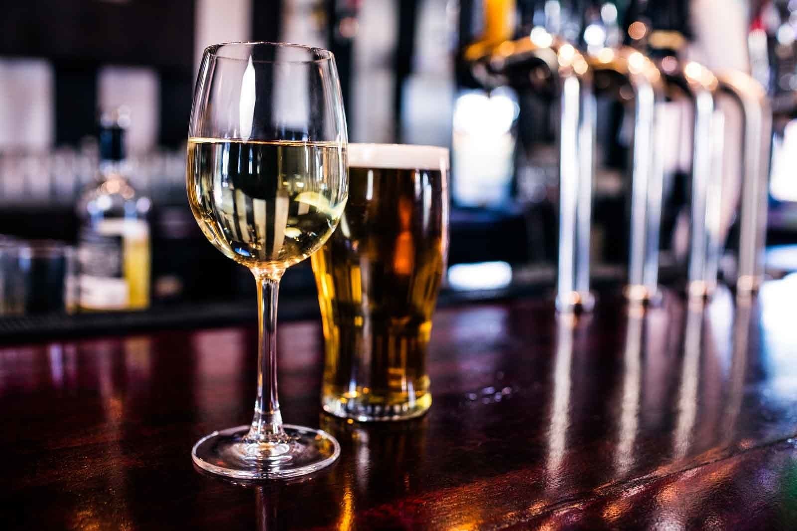 A glass of white wine next to a pint of beer on a bar counter.
