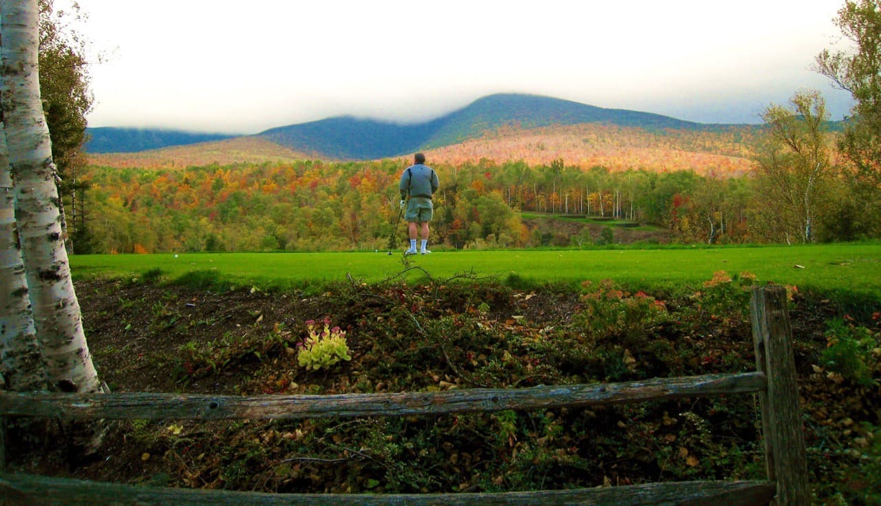A person stands on a grassy hill, gazing at a colorful mountain landscape.