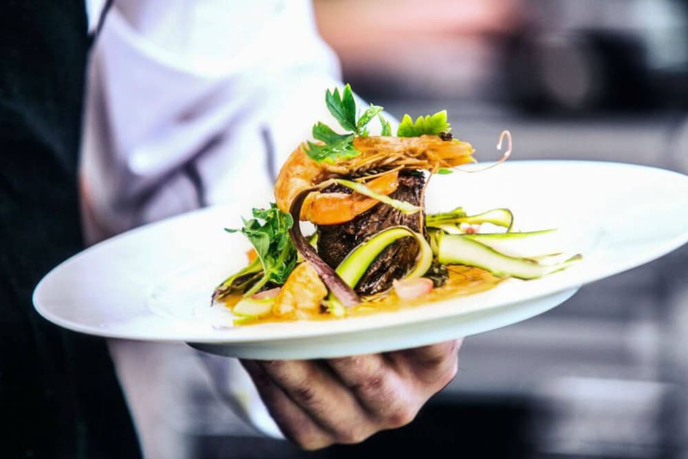 A gourmet dish featuring grilled shrimp, meat, and fresh greens on a white plate.