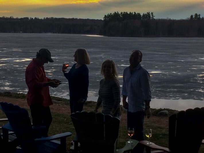 Silhouetted friends enjoying drinks by a frozen lake at sunset.