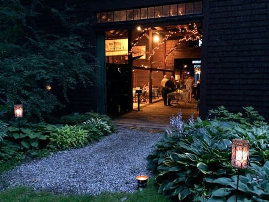 A softly lit pathway leads to an inviting barn interior with people mingling.