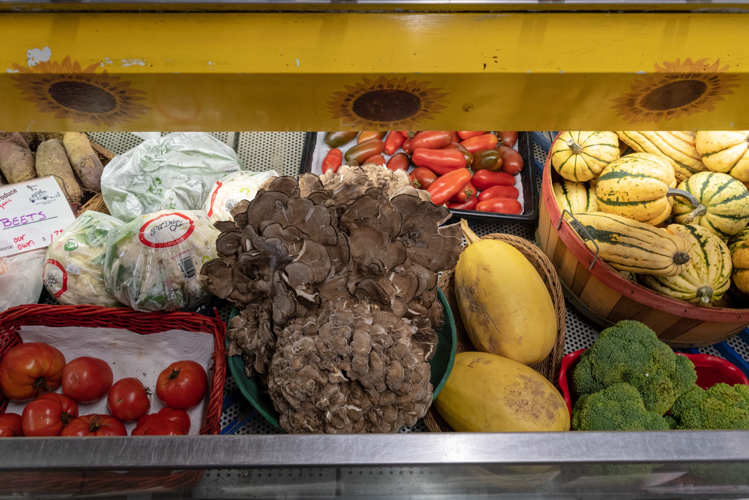 A variety of fresh produce including mushrooms, tomatoes, squash, and broccoli displayed in baskets at a market. A variety of fresh produce including mushrooms, tomatoes, squash, and broccoli displayed in baskets at a market.