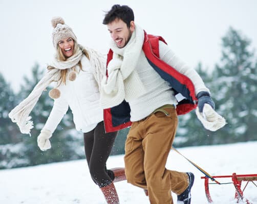 A smiling couple enjoys a snowy day, playfully pulling a sled together.