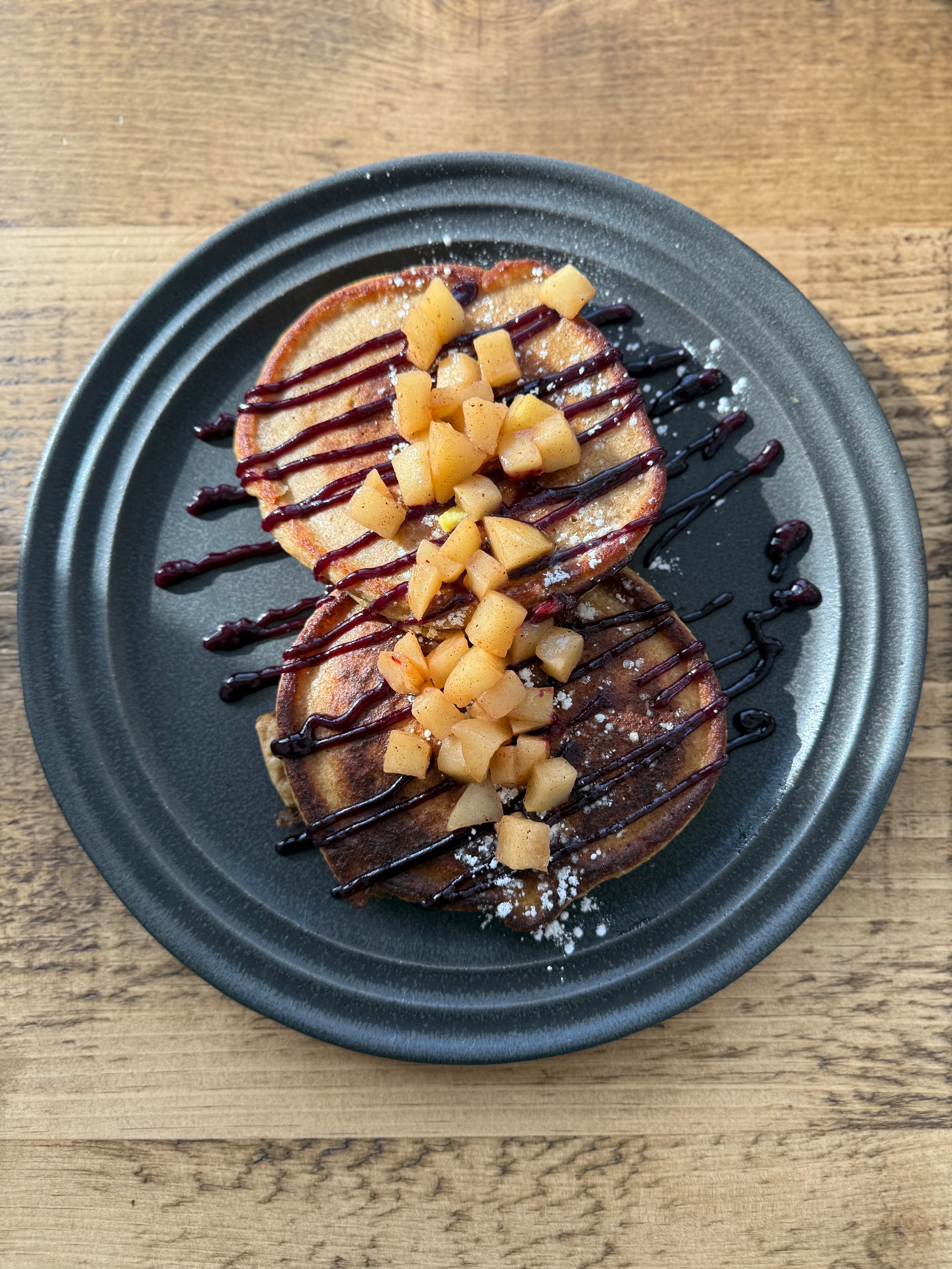 Two pancakes topped with diced apples and drizzled with chocolate sauce on a dark plate.