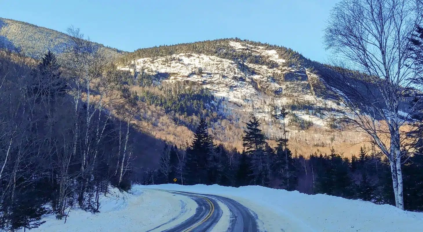 A winding road curves through a snowy landscape with towering mountains in the background.