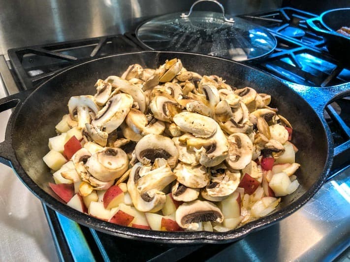 Sliced mushrooms and diced red potatoes are cooking together in a skillet on a stovetop.