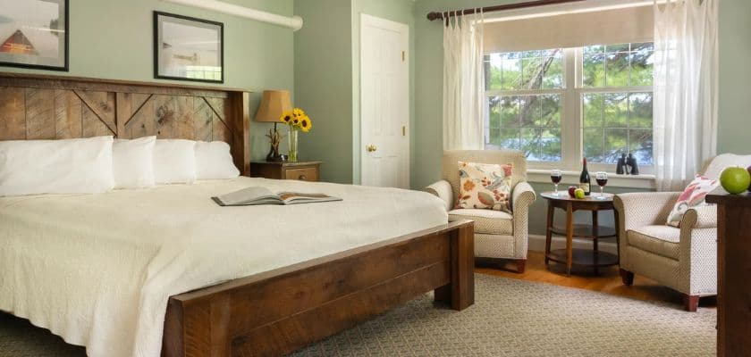 A cozy bedroom featuring a large bed, two armchairs, and a window with natural light.
