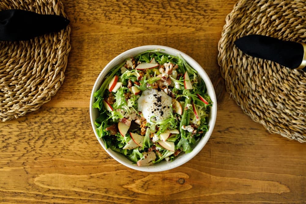 A fresh salad with greens, sliced apples, and a poached egg served in a bowl.