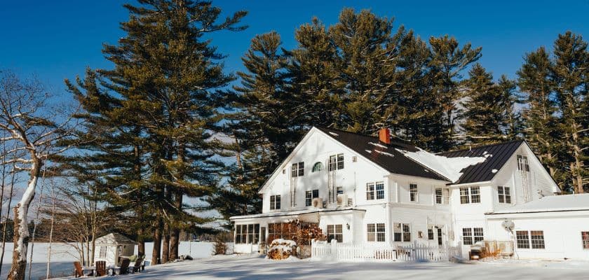 A white house surrounded by tall pine trees and snow.