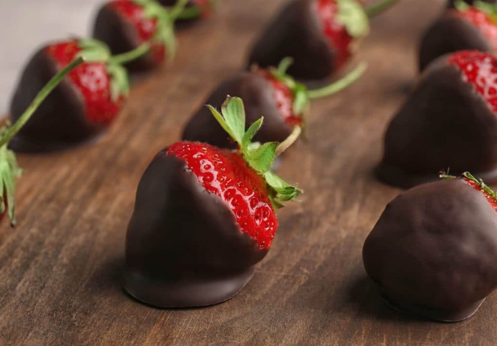 A row of chocolate-covered strawberries arranged on a wooden surface.