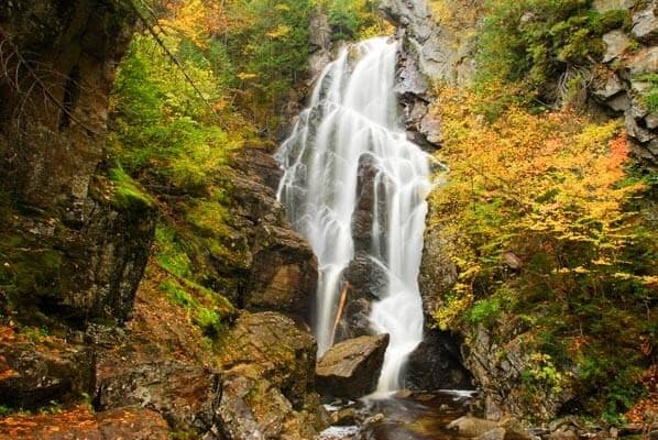A cascading waterfall surrounded by autumn foliage and rocky terrain.