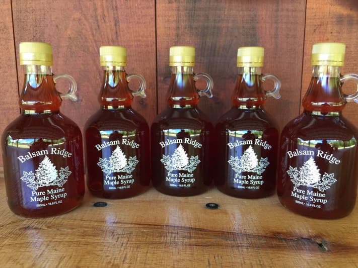 Five bottles of Balsam Ridge Pure Maine Maple Syrup arranged in a row on a wooden surface.