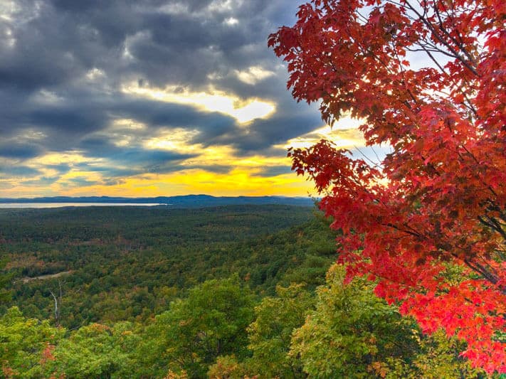 A vibrant autumn landscape with colorful foliage under a dramatic, cloudy sunset sky.