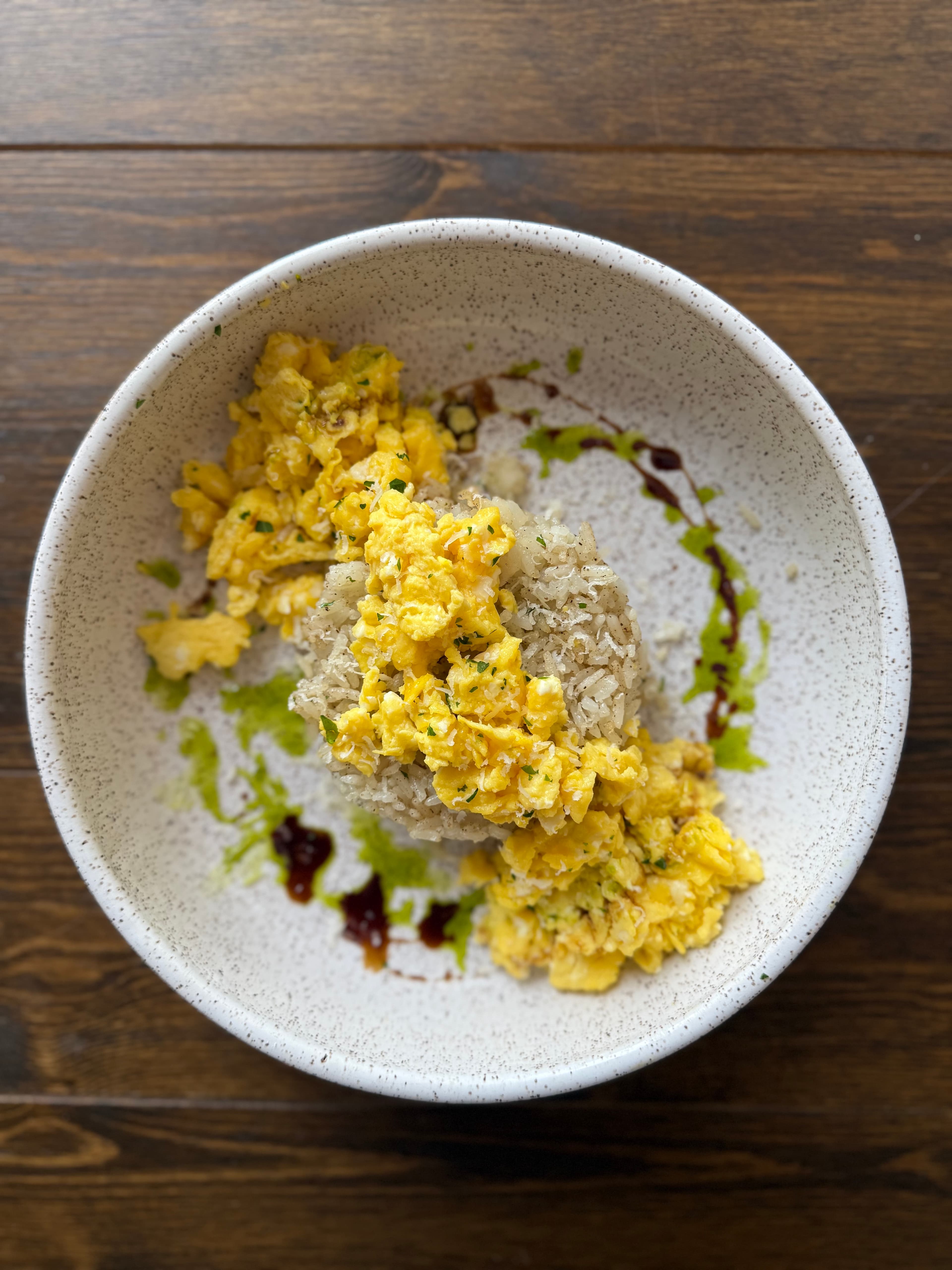A bowl of fluffy scrambled eggs served over a mound of rice, garnished with sauces.