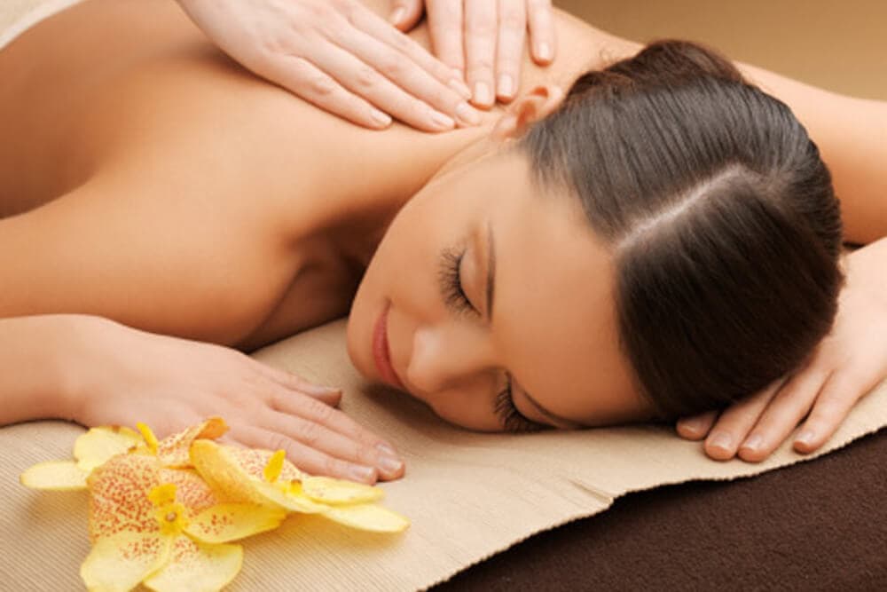 A woman relaxes during a massage with flowers nearby.