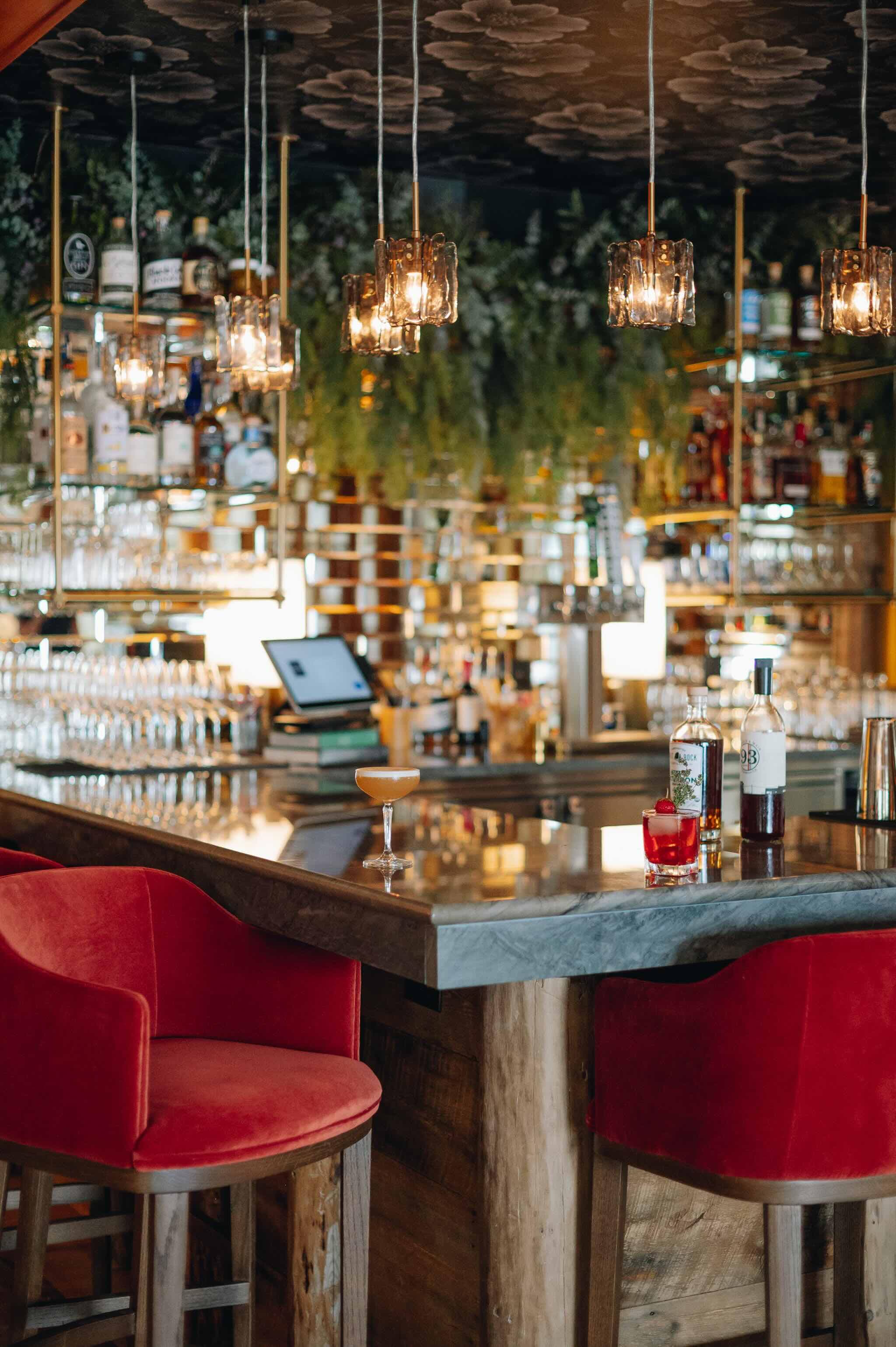 A stylish bar featuring red chairs, a marble countertop, and shelves stocked with various bottles.