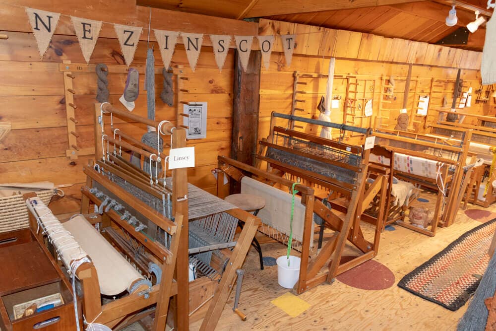 A weaving workshop featuring multiple looms and wooden walls with decorative bunting.