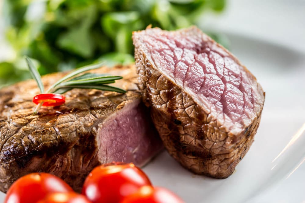 A close-up of a perfectly cooked steak with a garnish of rosemary and cherry tomatoes.