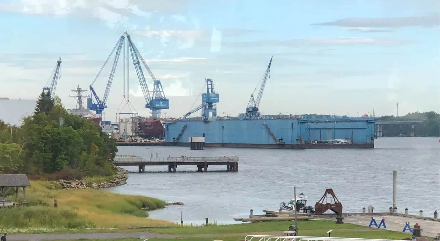 View of a harbor with cranes and a shipyard in the background.