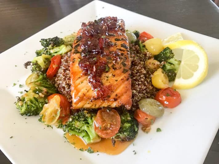 Grilled salmon topped with a glaze, served on a bed of quinoa and mixed vegetables.
