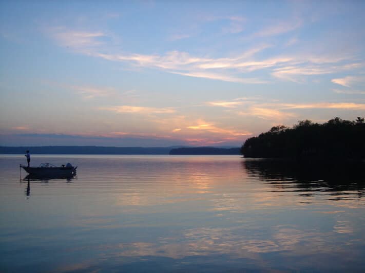 A serene lake at sunset with a lone fisherman in a boat.