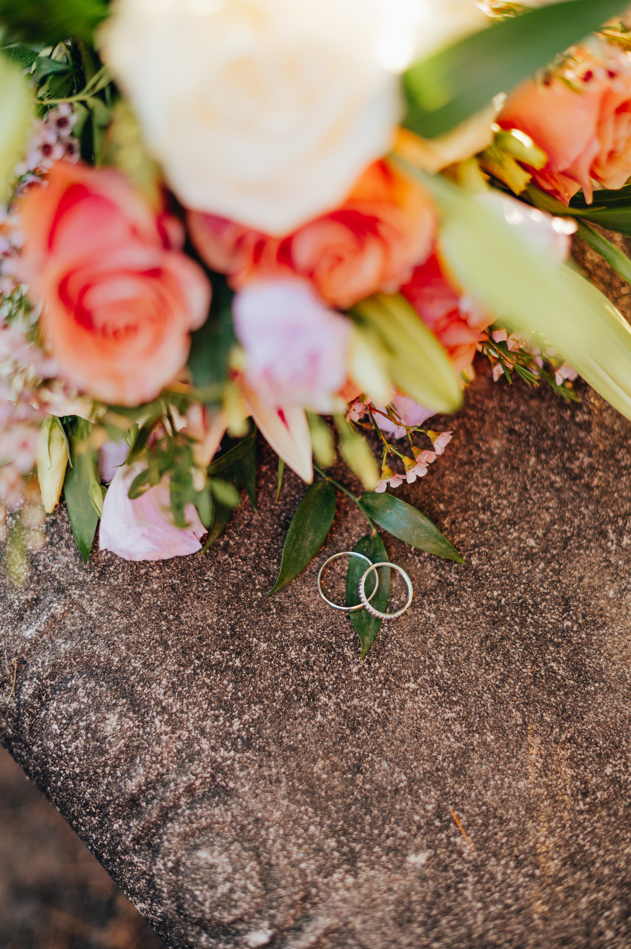 Two wedding rings surrounded by a bouquet of colorful flowers on a stone surface.