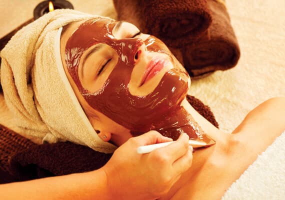 A woman relaxes with a chocolate facial mask in a spa setting.