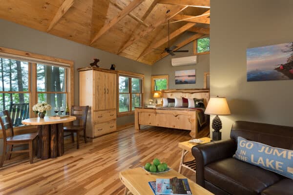 Cathedral ceiling in open concept cabin with sitting area, bistro table and king bed with expansive views.