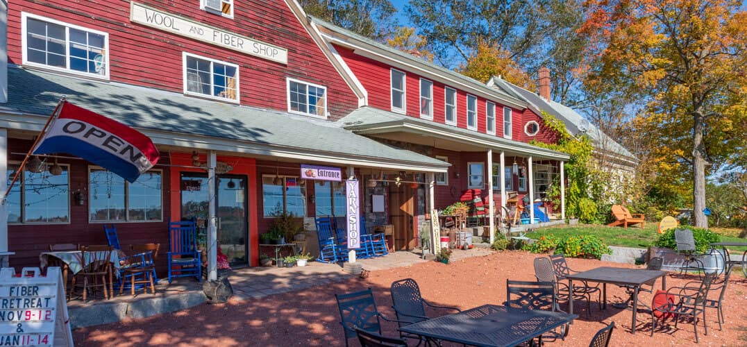 A red-paneled wool and fiber shop with outdoor seating, surrounded by colorful autumn foliage. A red-paneled wool and fiber shop with outdoor seating, surrounded by colorful autumn foliage.