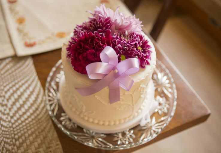 A decorated cake topped with colorful flowers and a purple ribbon, resting on a decorative plate.
